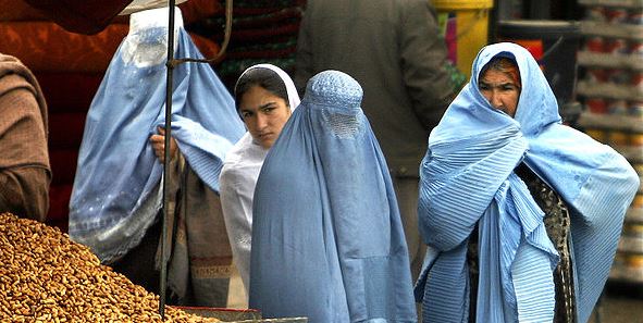 Afghan women interrupt their shopping to watch a photographer.