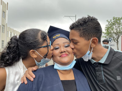 Une étudiante adulte est félicitée par ses deux enfants lors de la cérémonie de remise de son diplôme de bachelière