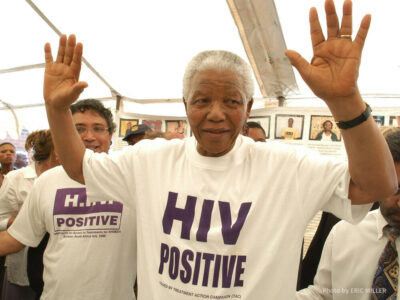 In December 2002, former South African president Nelson Mandela accepted the offer of a beneficiary of the project and changed his shirt for an HIV-Positive T-shirt. See Zackie (Zackie Achmat of the Treatment Action Campaign, a South African NGO {TAC},) just behind.
