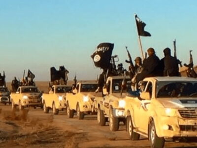 Militants of the Islamic State group hold up their weapons and wave flags on their vehicles in a convoy on a road leading to Iraq, while riding in Raqqa, Syria.