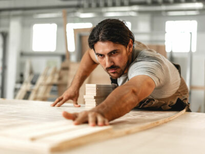 Young carpenter man looking and choosing wood plank at workshop in carpenter wood factory close up