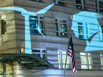 Projektion auf der Fassade der US-Botschaft. Zu sehen ist das Konterfei des US-Präsidenten Donald Trump, dem ein Windrad ins Gesicht bläst.